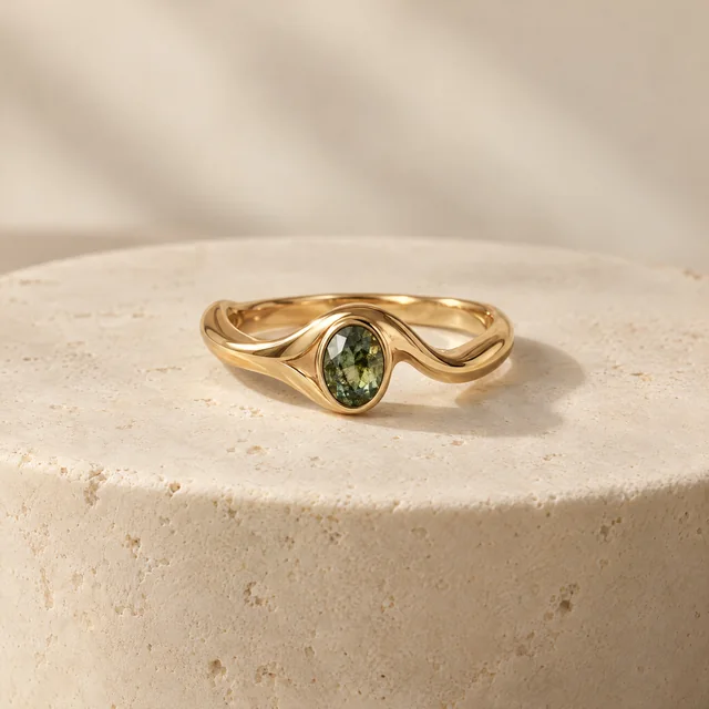 Ein Goldring-Entwurf mit einem grรผnen Edelstein auf einem elfenbeinfarbenen Sockel
